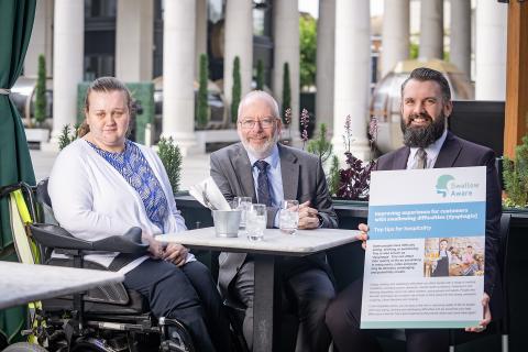 Photo show three people at a restaurant table one holding cover of the Swallow Aware Factsheet