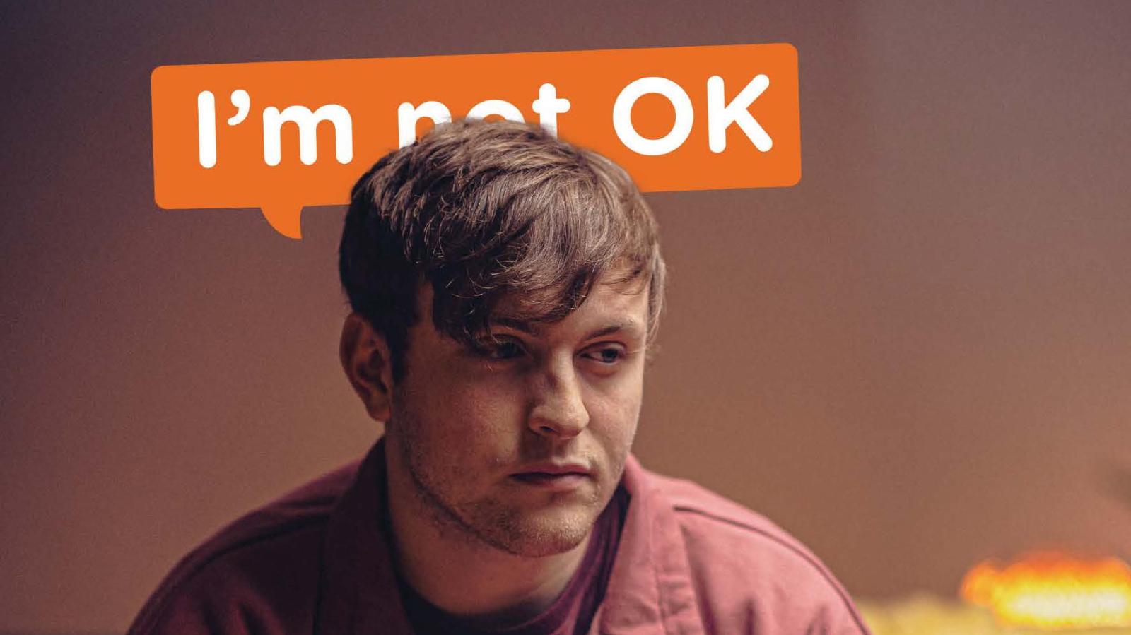 A man with text behind him that says I'm not ok" with the word "not" obscured by the man's head